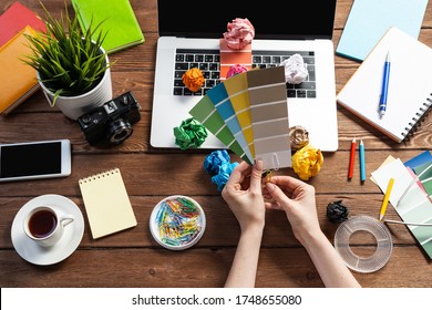 Interior Designer Choosing Colors From Swatches At Wooden Desk. Office Workplace With Laptop And Stationery. Selection Of Color Palette For Design. Professional House Renovation And Interior Redesign.