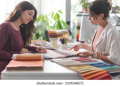 Interior designer and customer sitting at office desk, they are checking fabric swatches and picking colors - Powered by Shutterstock