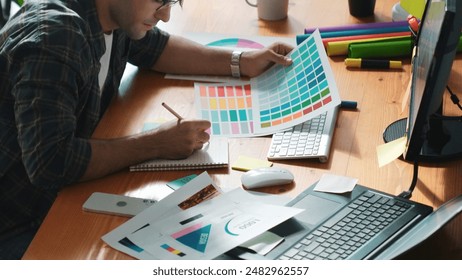 Interior designer looking at laptop and designing color while looking at palette at meeting table with laptop, computer and paper placed. Close up of business man working on color design. Symposium. - Powered by Shutterstock