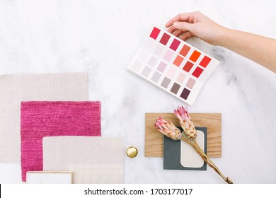 Interior Designer Selecting Paint Colors, Fabric Swatches, And Remodel Design Samples. Overhead Sample Board Lay Down On White Marble Surface With Pink Color Story