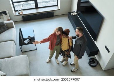 Interior designer showing modern living room design to excited couple. They are discussing renovation plans, standing in stylish apartment with large TV and comfortable furniture - Powered by Shutterstock