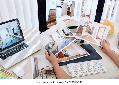 Interior Designer Sitting At Desk And Looking At Printed Photos Of Clients Rooms After Renovation