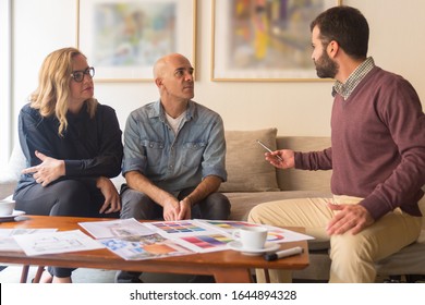 Interior Designer Talking With Clients At Home. Focused Woman And Men Sitting In Living Room At Home And Talking. Renovation Concept