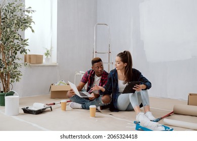 Interior Designers Construction Managers Architects Work In Newly Constructed Apartment Building Apartment Renovation Young Woman And Co-worker Sit On Floor With Mugs Of Coffee Laptop Tablet Plan