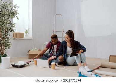 Interior Designers Construction Managers Architects Work In Newly Constructed Apartment Building Apartment Renovation Young Woman And Co-worker Sit On Floor With Mugs Of Coffee Laptop Tablet Plan