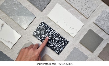 interior designer's hand selecting material samples palette contains various type, texture and color of artificial stones, marbles, grainy stone tiles, quartzs placed on grey travertine background. - Shutterstock ID 2215147851