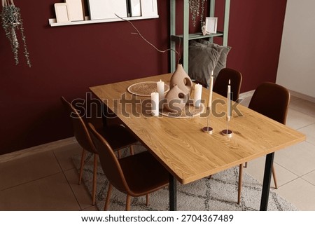 Interior of dining room with shelving unit, chairs, houseplants and candle holders on table near burgundy wall