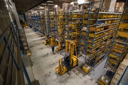 Interior of a distribution warehouse viewed from above. View onto blue storage racks and yellow boxes. Logistics and warehousing in full action with forklift and a lot of goods around, an Industrial Photo by Anze Furlan