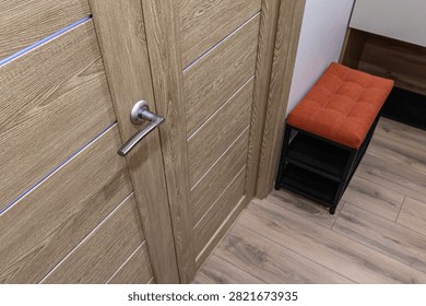 light‑oak interior door with horizontal panels and subtle blue accent lines. next to it stands a compact bench with an orange tufted cushion and a black metal frame