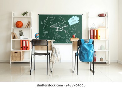 Interior of empty classroom with blackboard, shelf units and desks