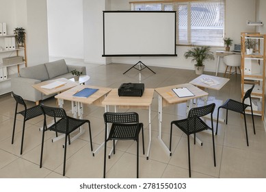 Interior of empty classroom with blank projector screen and desks