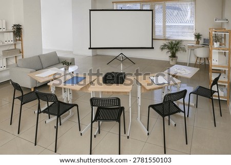 Interior of empty classroom with blank projector screen and desks
