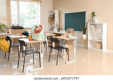 Interior of empty classroom with chalkboard, shelf units and desks