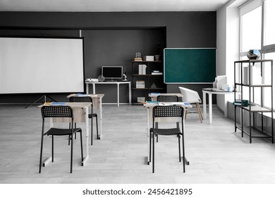 Interior of empty classroom with desks, projector screen and chalkboard - Powered by Shutterstock