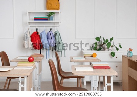 Interior of empty classroom with school desks and backpacks hanging on hooks