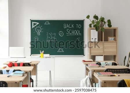 Interior of empty classroom with school desks and text BACK TO SCHOOL on chalkboard