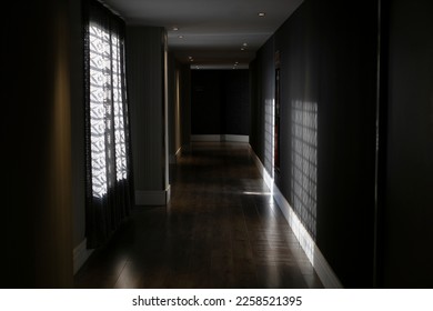 Interior of empty dark hallway with gray walls and curtained windows and wooden floor with sunrays
