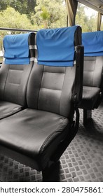 Interior of an empty passenger bus with rows of black seats covered by blue headrest covers.