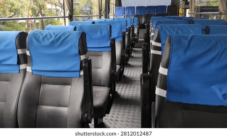 Interior of an empty passenger bus with rows of black seats covered by blue headrest covers.