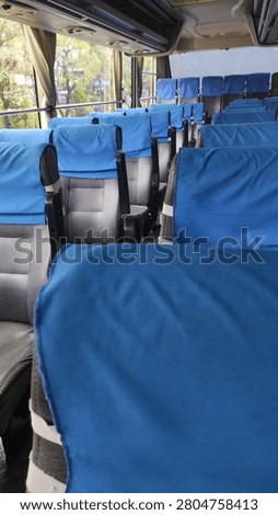 Interior of an empty passenger bus with rows of black seats covered by blue headrest covers.
