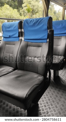 Interior of an empty passenger bus with rows of black seats covered by blue headrest covers.
