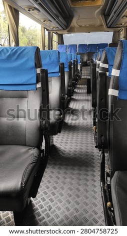 Interior of an empty passenger bus with rows of black seats covered by blue headrest covers.