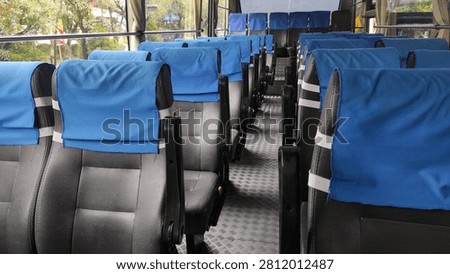 Interior of an empty passenger bus with rows of black seats covered by blue headrest covers.