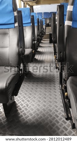 Interior of an empty passenger bus with rows of black seats covered by blue headrest covers.