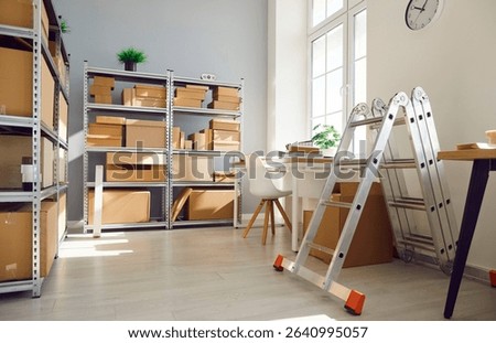 Interior of empty work space with office desk in warehouse with shelves filled cardboard boxes of retail products. Business workplace used for shipping merchandise and stock inventory.