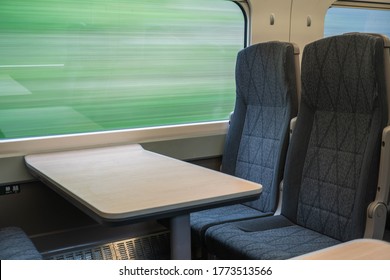 Interior of fast moving train showing seats and table with blurred out countryside background seen through the window