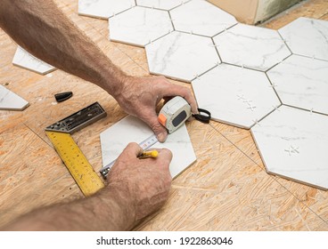 Interior finishing worker (tiler) laying white hexagon ceramic gres tiles on the floor. Bathroom renovation works. Handyman at work.