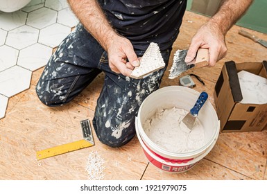 Interior finishing worker (tiler) spreading adhesive (glue) before laying ceramic gres tiles on the floor. Bathroom renovation works. Handyman at work.