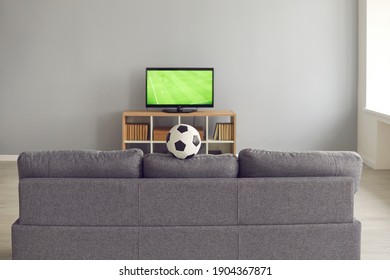 Interior Of Football Fan's Living-room. Back View Of Grey Sofa In Rec Room For Leisure, Relaxation And Watching Sport TV Channels. Empty Living Space With Couch, Soccer Ball And New Television Set