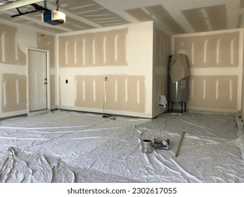 Interior of a garage with raw drywall walls about to be painted. Painters drop cloths are spread out on the floor to keep the paint from getting on the concrete.