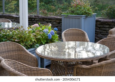 Interior Of Green Outdoor Terrace At Restaurant Or Hotel In City Garden, Park Or Forest With No People. Rattan Wicker Table And Chairs In Street Cafe Decorated With Summer Blooming Flowers And Plants