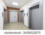 An interior hallway with two elevators, an exit door framed by brick, and tile flooring