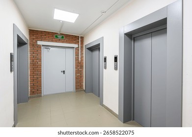 An interior hallway with two elevators, an exit door framed by brick, and tile flooring