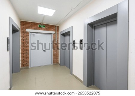 An interior hallway with two elevators, an exit door framed by brick, and tile flooring