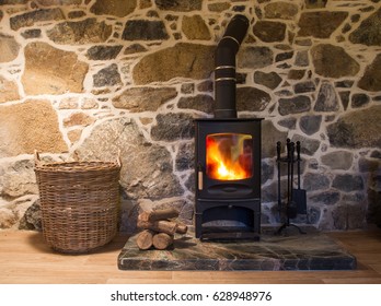 The interior and hearth of a stone walled cottage with a wood burner fireplace, hearth and storage basket for logs.