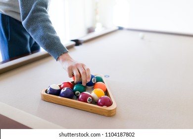 Interior House Home With Billiard Pool Table In Living Room, Young Man In Winter Cold Sweater Placing Balls Inside Triangle Rack, Setting Up Game