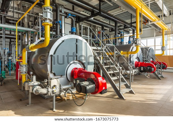 The interior of an\
industrial boiler room with three large boilers, many pipes, valves\
and sensors.