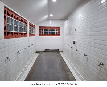 Interior of Islamic ablution area with rows of faucets. Clean white tiled room for Muslim wudu ritual purification before prayer in mosque facility with ventilation blocks.