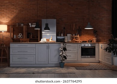 Interior of kitchen with counters, shelf units and glowing lamps at night