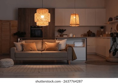 Interior of kitchen with counters, sofa and glowing lamps at night