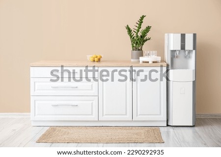 Interior of kitchen with modern water cooler near beige wall