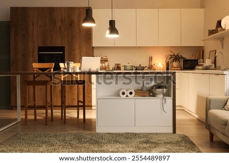 Interior of kitchen with table, counters and glowing lamps in evening