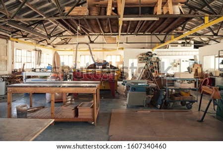 Interior of a large carpentry workshop full of workbenches and an assortment of tools, wood and machinery