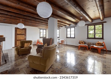 Interior of a large living and dining room with a fireplace. There is old and outdated furniture. A holiday home in the mountains