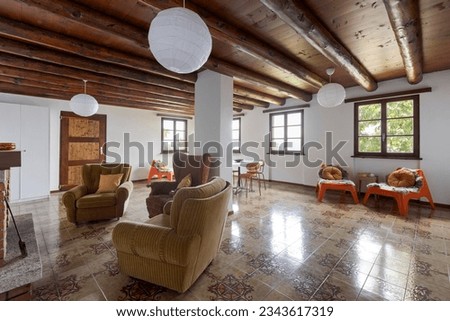 Interior of a large living and dining room with a fireplace. There is old and outdated furniture. A holiday home in the mountains