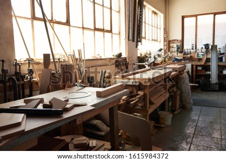 Interior of a large woodworking shop with workbenches full of an assortment of cut wood and tools